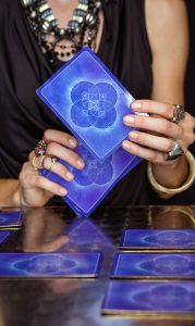 Tarot-Credits23-179×300 A woman holding a blue tarot card deck, practicing spiritual tarot reading for insights and guidance.